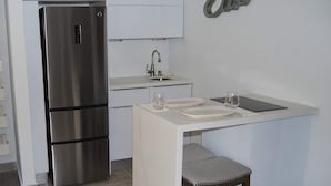 Une cuisine compacte équipée d’un réfrigérateur en acier inoxydable, d’un petit évier et d’un tabouret de bar.