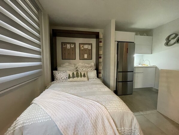 A bedroom with a bed, a small kitchenette, and a bathroom visible through an open door.