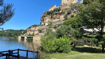 A historic castle on a hill overlooking a river, with a wooden dock and lush greenery.