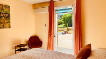 A hotel room with a bed, a chair, a small table, and a view of a garden through a sliding door.