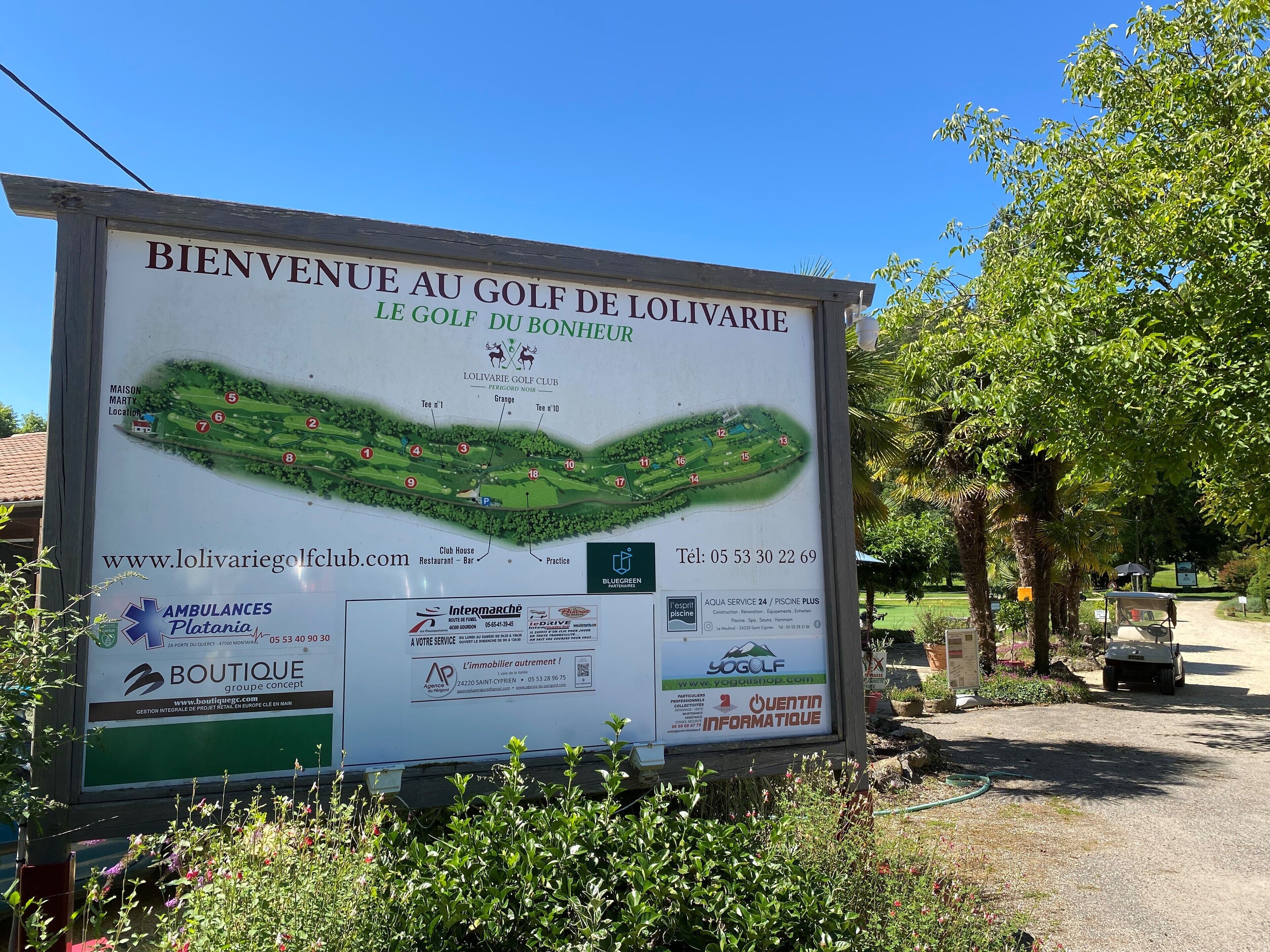 En välkomstskylt för golfklubben L'olivarie, med en karta över banan, kontaktuppgifter och diverse företagsannonser.