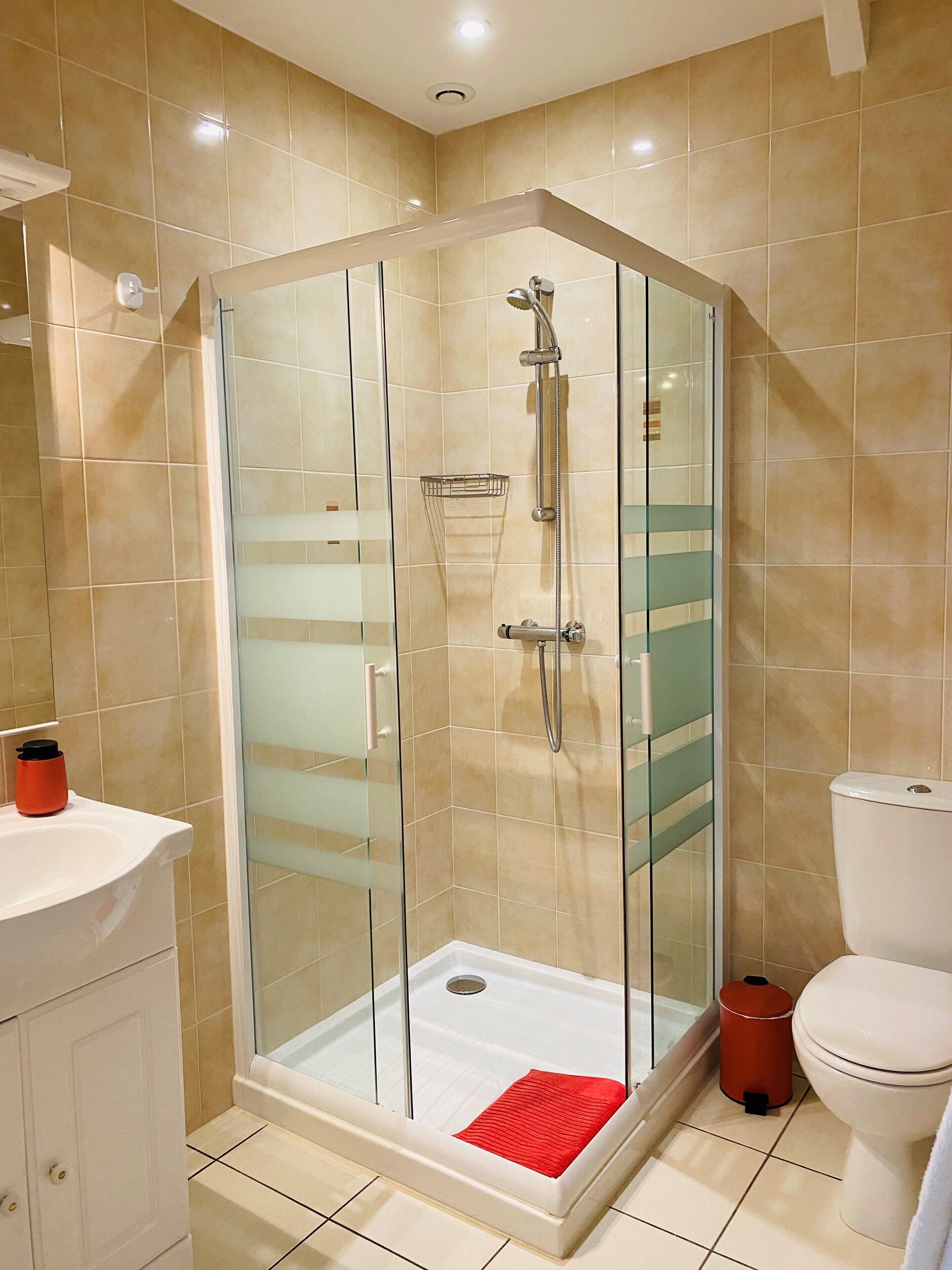 Een moderne badkamer met een douchecabine van glas, een wit toilet en een wastafel met een rode zeepbakje.