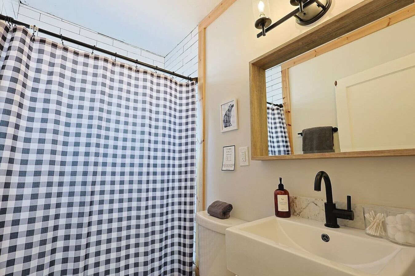 Een badkamer met een douchegordijn met ruitpatroon, een wastafel met een zeepfles en een spiegel boven de wastafel.