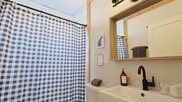 Een badkamer met een douchegordijn met ruitpatroon, een wastafel met een zeepfles en een spiegel boven de wastafel.