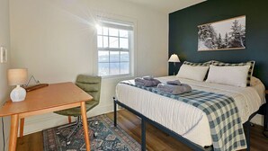 Een slaapkamer met een bed, een bureau, een stoel, een raam en een schilderij aan de muur.