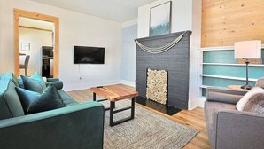Een moderne woonkamer met een open haard, een flatscreen televisie aan de wand en een houten salontafel.