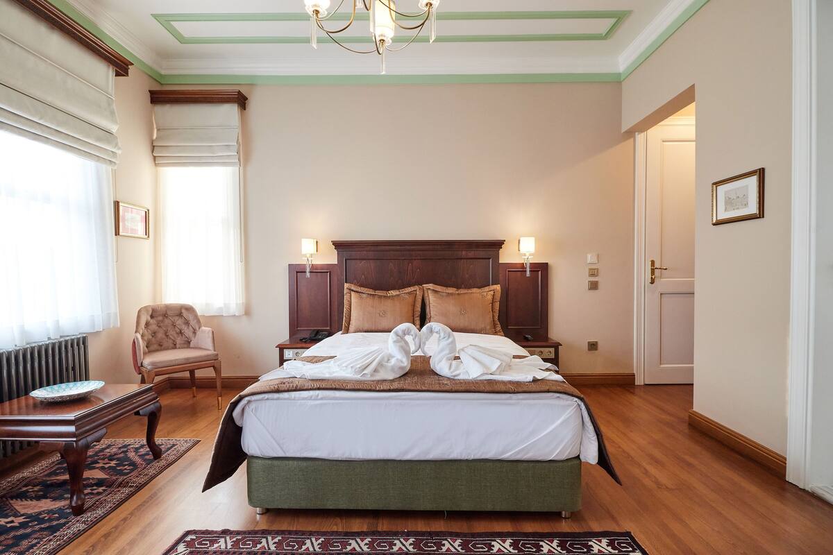 Ein ordentlich eingerichtetes Hotelzimmer mit einem großen Bett, zwei Nachttischlampen, einem Sessel und einem kleinen Tisch.