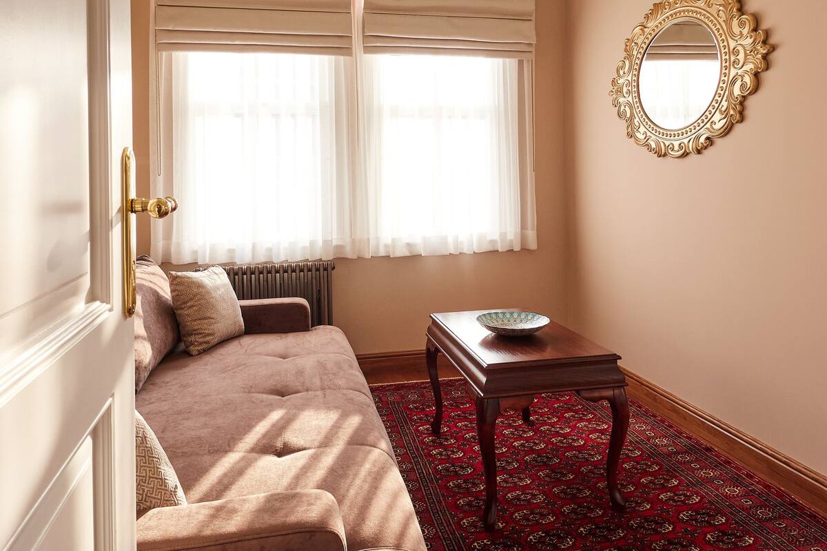 Ein Zimmer mit einer Couch, einem Tisch mit einer Schüssel, einem Spiegel und einem gemusterten Teppich.