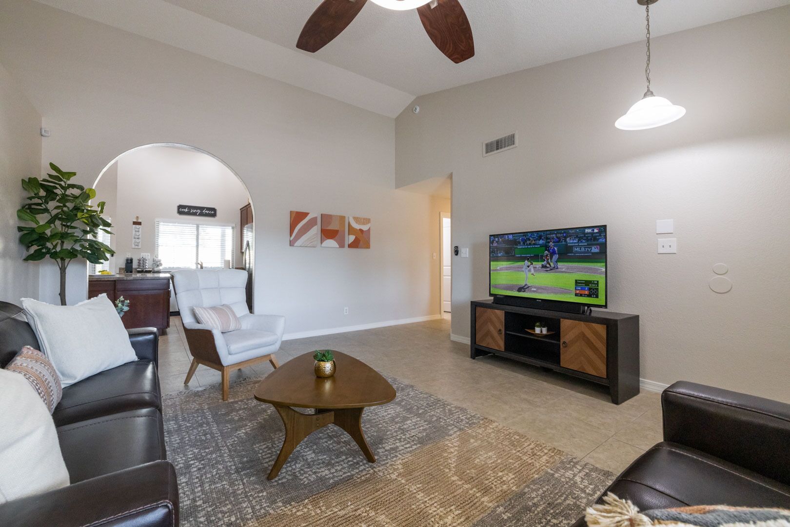 A living room with a flat-screen TV, leather sofas, a coffee table, and a ceiling fan.