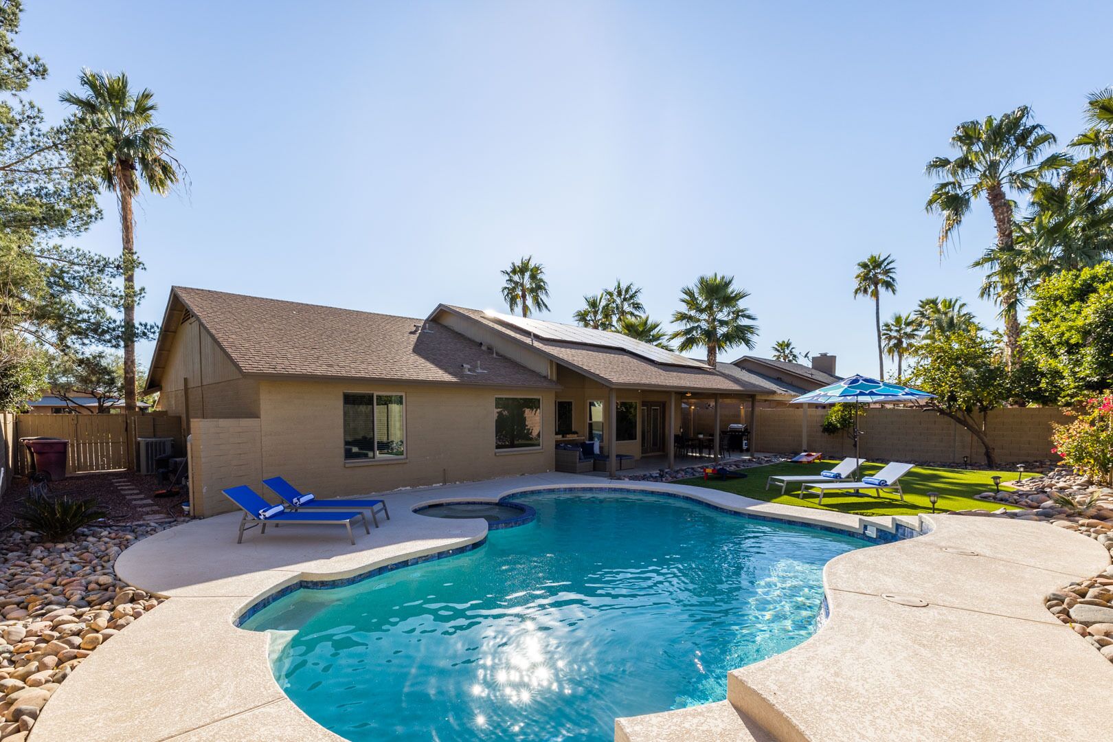 Une maison avec une piscine, un patio couvert et une pelouse agrémentée de palmiers.