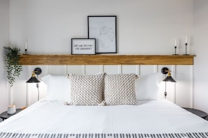 Een keurig opgemaakt slaapkamer met een houten hoofdbord, twee bedlampen, een lijst met een citaat en een decoratieve plant.