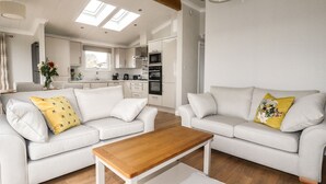 A modern living room with a sofa set, a wooden coffee table, and a kitchen in the background. - Acorn Lodge (Redruth)