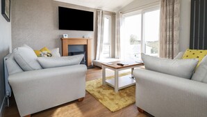 A living room with two grey sofas, a wooden coffee table, a fireplace, and a flat-screen TV mounted on the wall. - Acorn Lodge (Redruth)