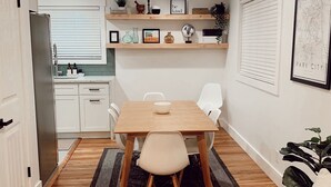 Een moderne keuken met witte kasten, een houten aanrecht en een inbouwoven. Er is een eethoek met een houten tafel, witte stoelen en een vloerkleed.