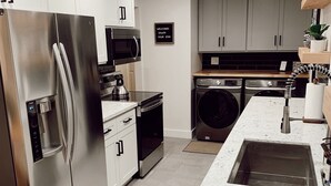 Een moderne keuken met roestvrijstalen apparatuur, een inbouwoven, magnetron en vaatwasser. Er is een granieten aanrechtblad en een spoelbak met een kraan.