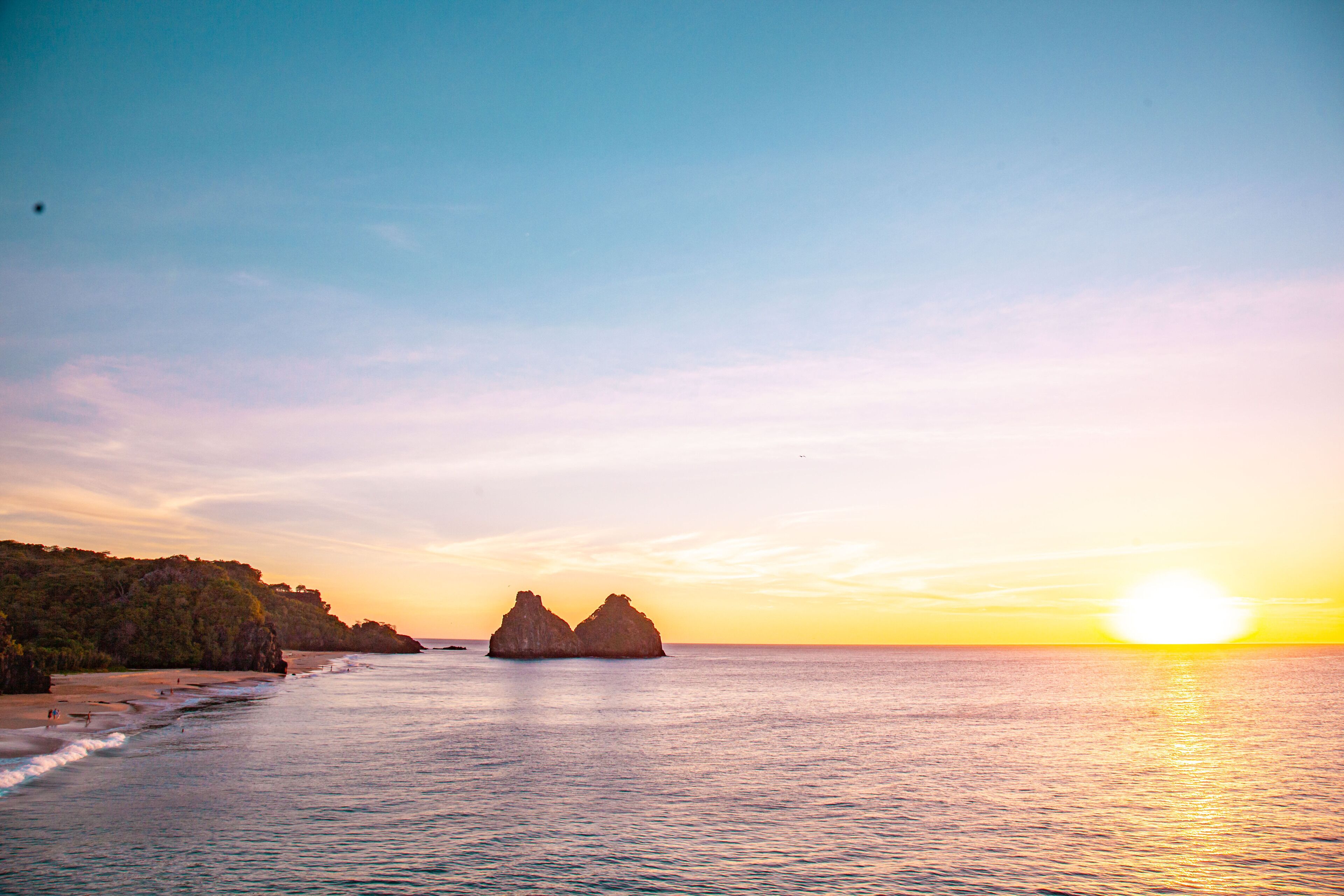 A coastal landscape with a clear sky, calm sea, and rocky formations.
