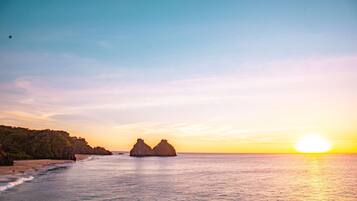 A coastal landscape with a clear sky, calm sea, and rocky formations.