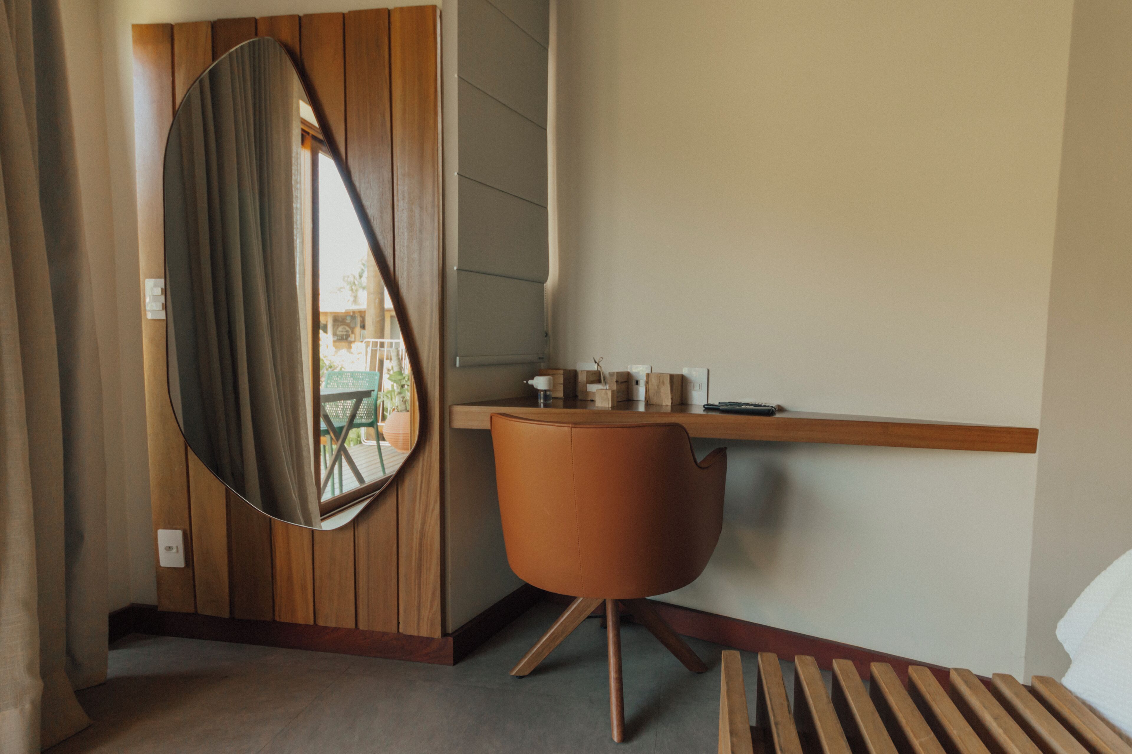 A hotel room with a wooden desk, a round mirror, a brown chair, and a bed.