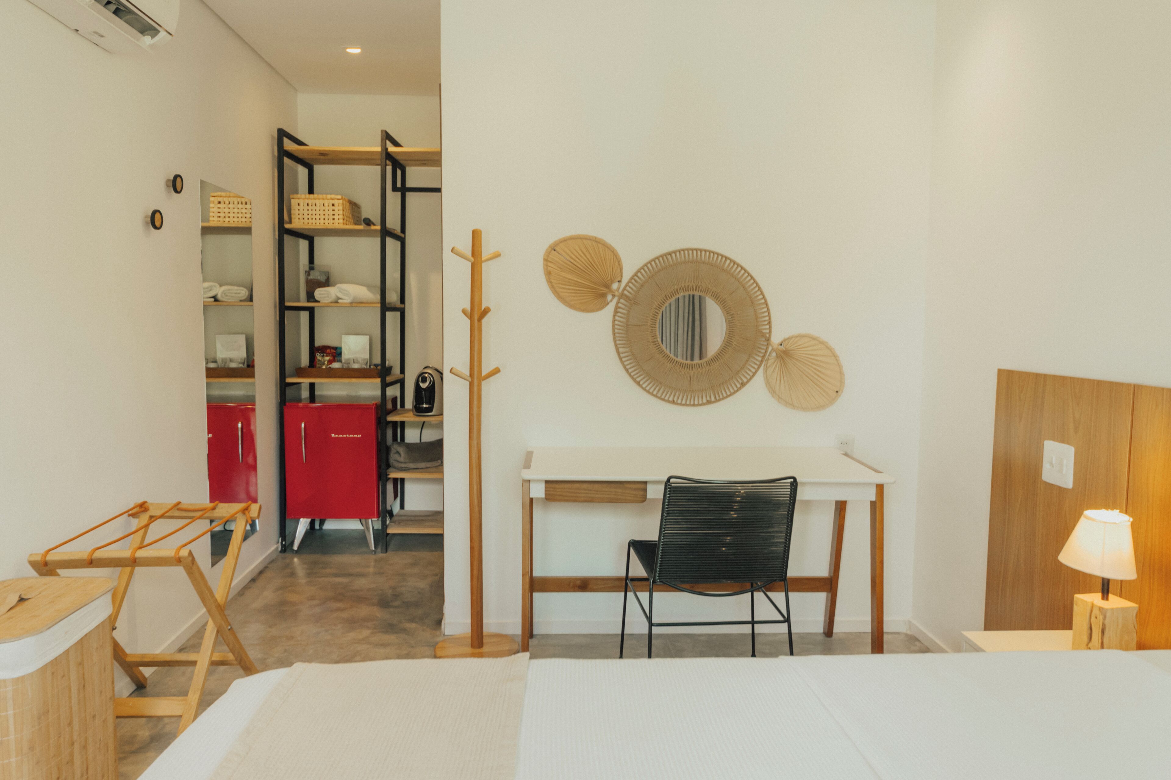 A room with a bed, a desk with a chair, a wardrobe, a coat rack, and a wall with decorative items.