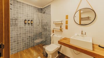 Kylpyhuoneessa on laatoitettu suihku, wc, peilillä varustettu pesuallas ja puiset hyllyt.