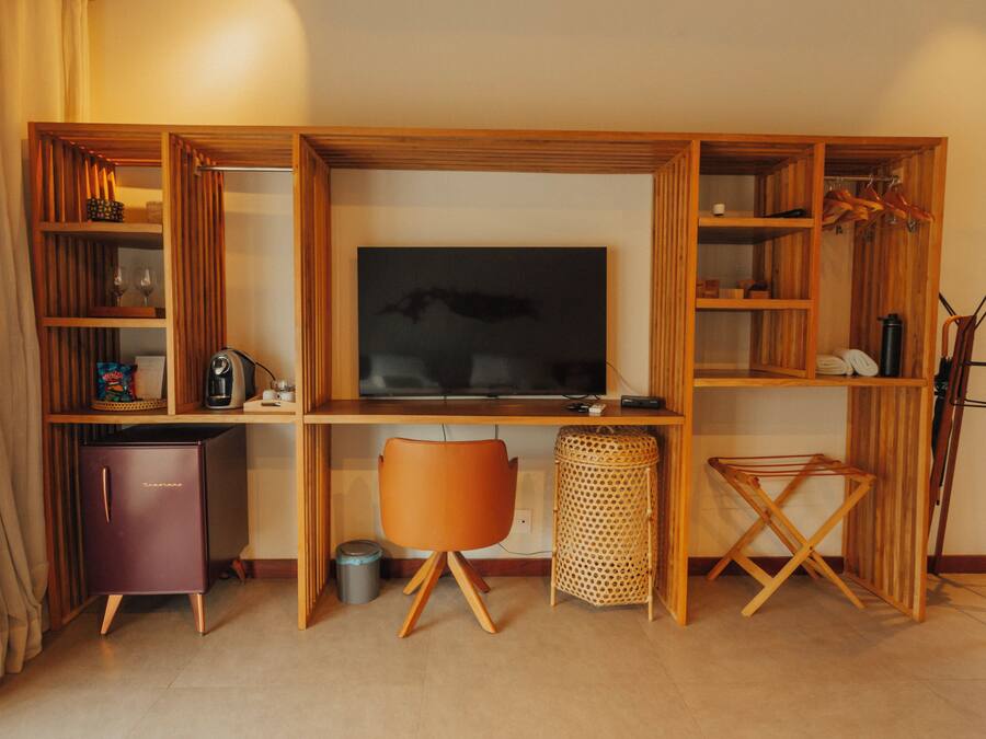 Una sala moderna con un televisor de pantalla plana, estanterías de madera, un mueble pequeño, una cesta de mimbre y un tendedero.