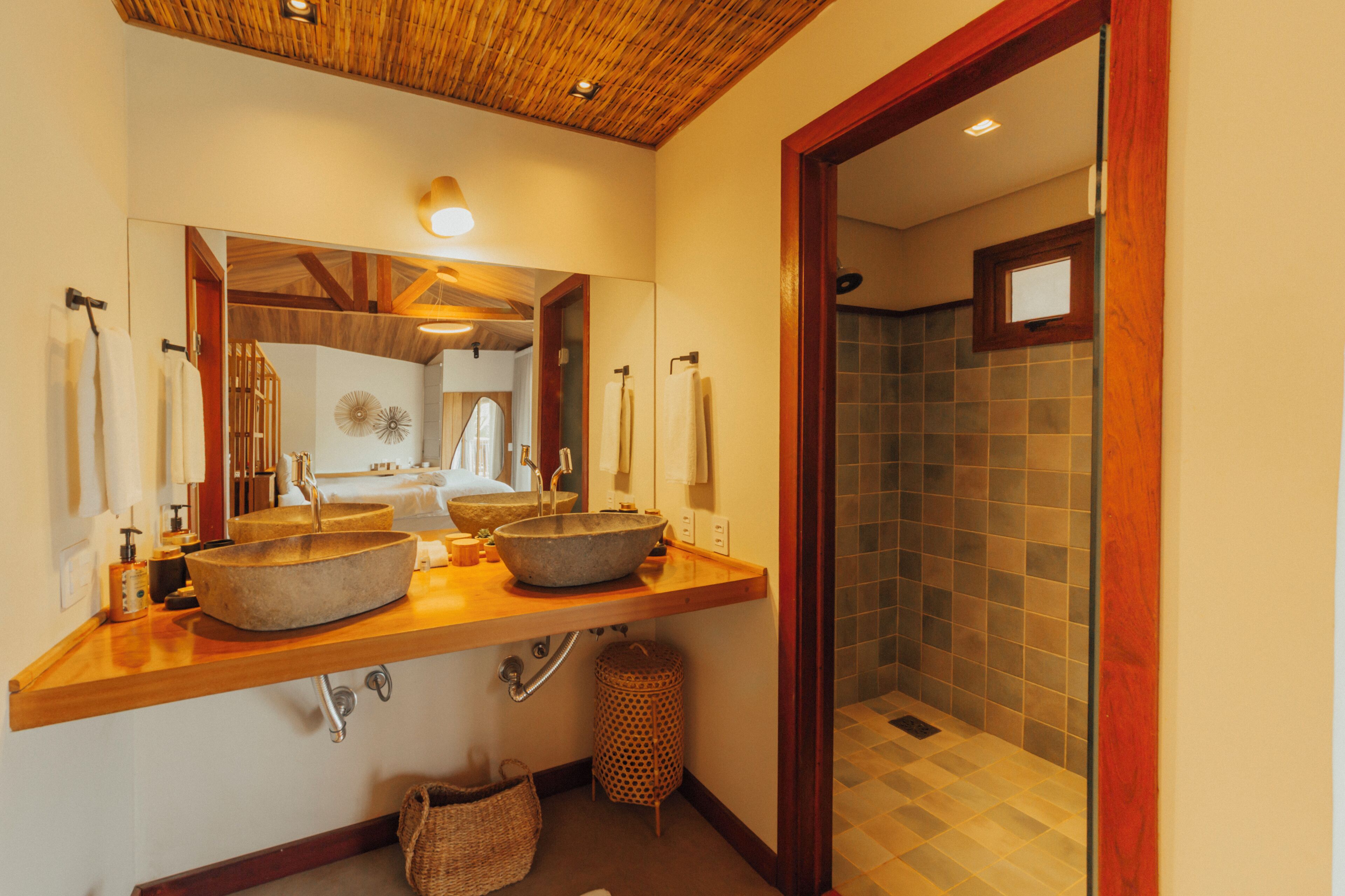 A bathroom with two large stone sinks, a wooden vanity, a mirror, and a shower area with tiled walls.