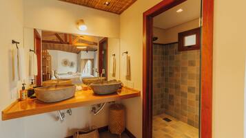 Un baño con dos lavamanos de piedra, un mueble de tocador de madera, un espejo y una zona de ducha con paredes de azulejos.