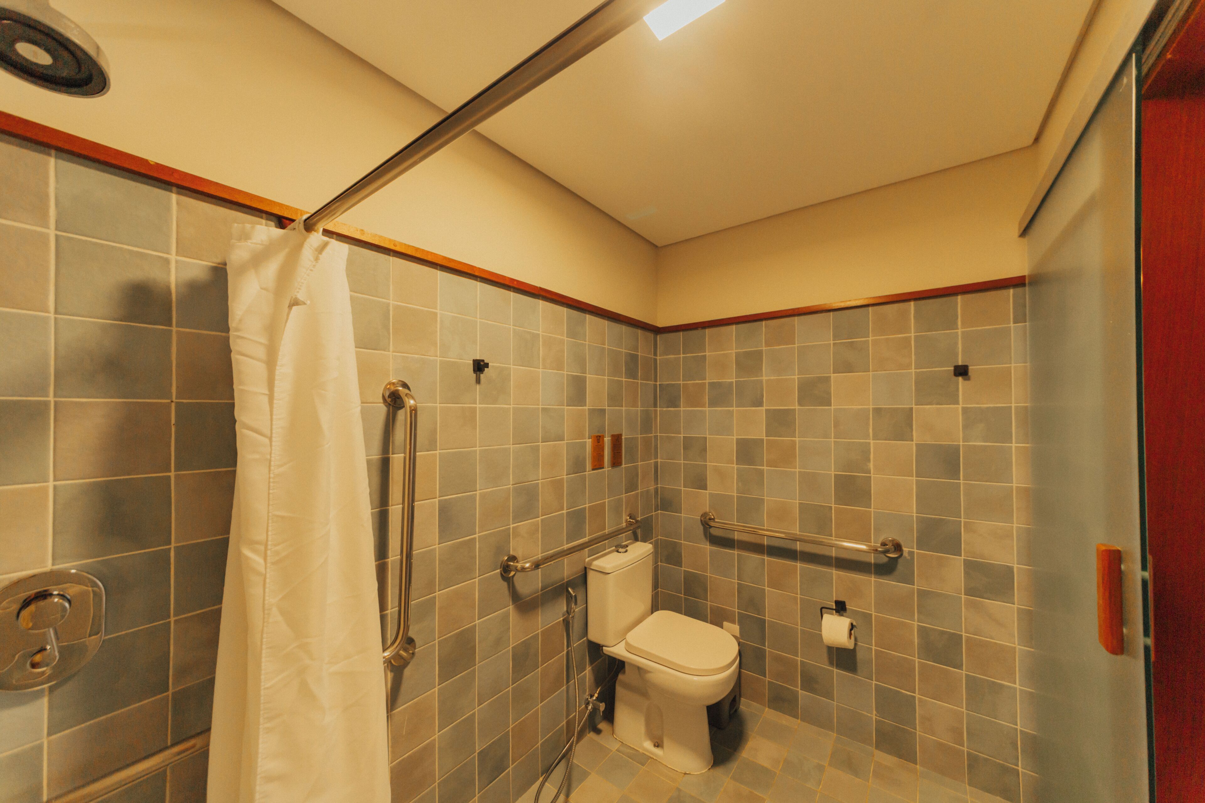 A small bathroom with a shower, toilet, and grab bars.