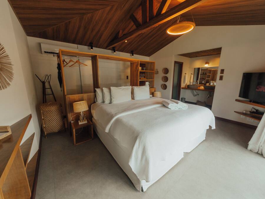 A bedroom with a large bed, wooden ceiling beams, a TV, and a mirror.