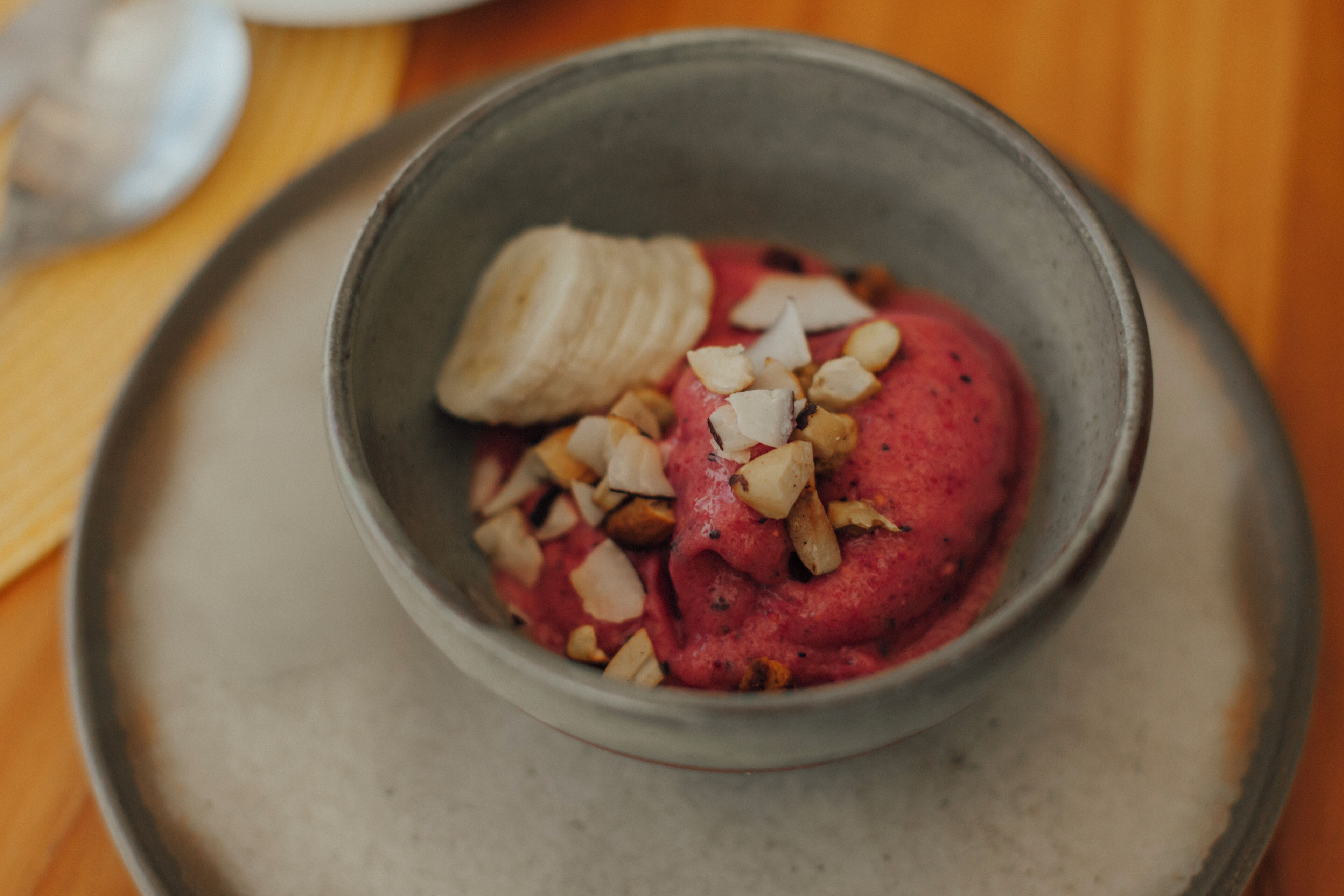 A bowl of food with a smooth texture and a reddish hue, topped with sliced almonds.