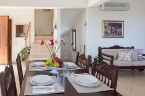A dining area with a table set for four, a fruit bowl, and a sofa in the background.