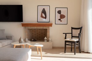 A living room with a fireplace, a sofa, a coffee table, and a chair. There are two framed artworks on the wall above the fireplace.