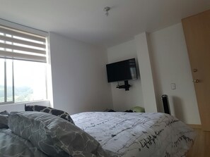 A bedroom with a bed, a television mounted on the wall, and a window with blinds.