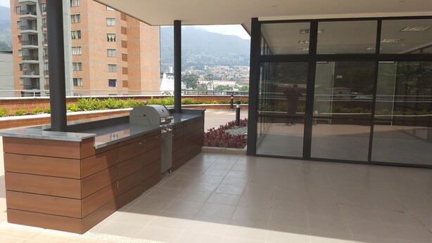 Une terrasse sur le toit équipée d’un barbecue, de meubles en bois et d’une porte vitrée donnant accès à un espace de détente extérieur.
