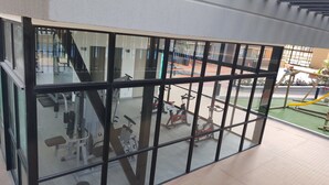 Une salle de sport équipée de matériel d’exercice, un espace extérieur verdoyant et une vue sur un bâtiment doté d’un escalier.