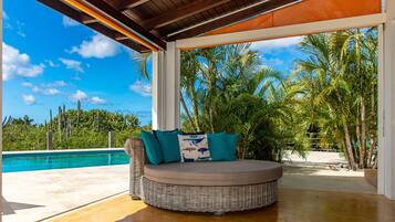 A covered outdoor seating area with a view of a pool and palm trees.