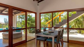 A dining area with a table, chairs, and a view of a pool and palm trees through large glass doors.
