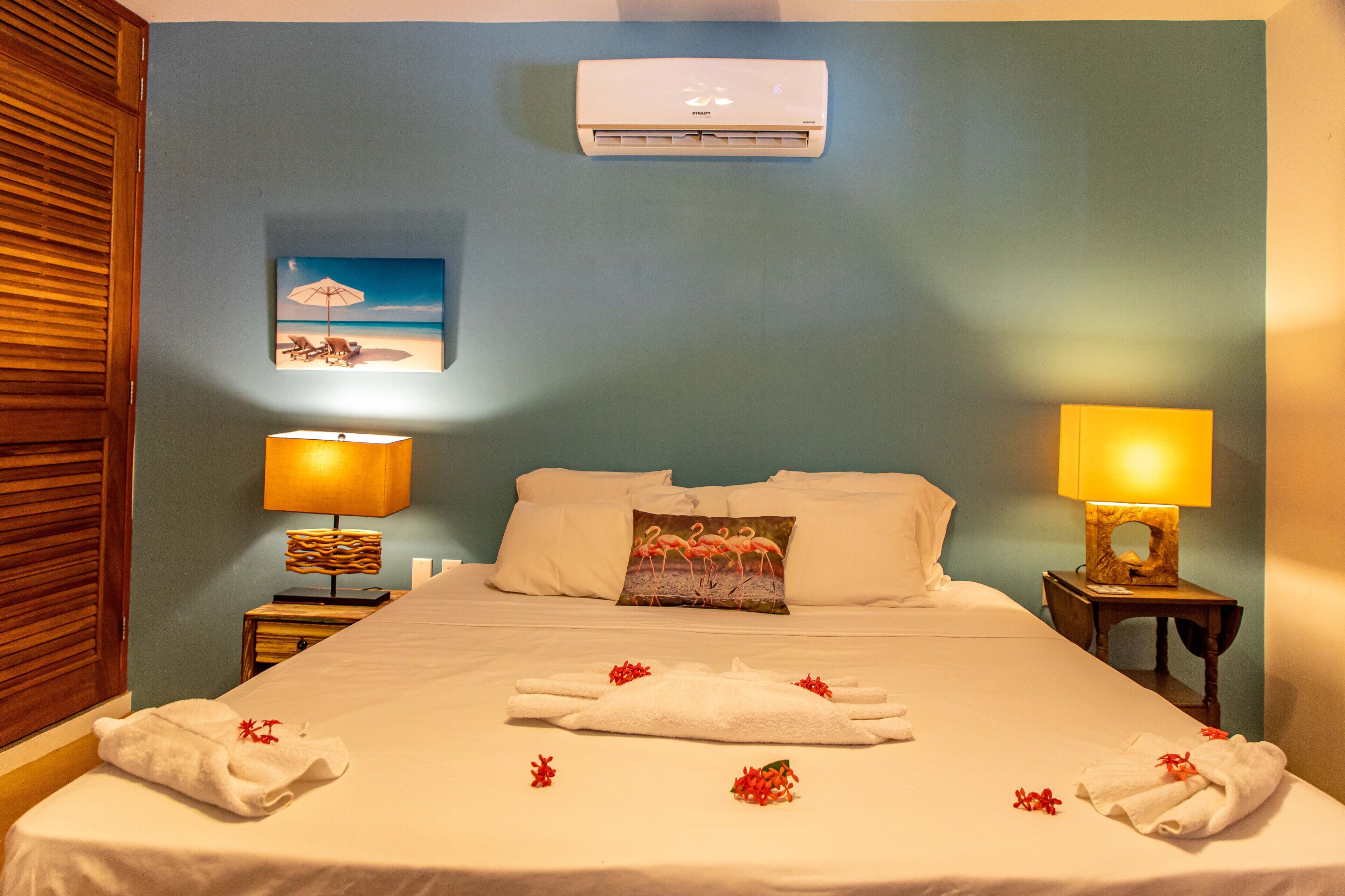 A hotel room with a bed, two nightstands with lamps, a wall-mounted air conditioner, and a beach-themed painting.