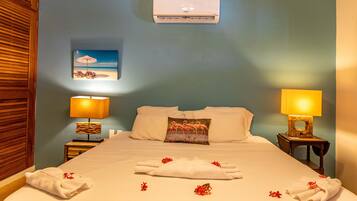A hotel room with a bed, two nightstands with lamps, a wall-mounted air conditioner, and a beach-themed painting.