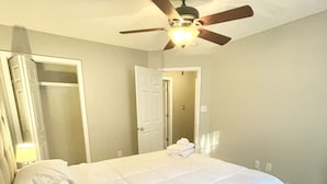 Une chambre à coucher avec un lit, un ventilateur de plafond et une porte donnant sur une autre pièce.