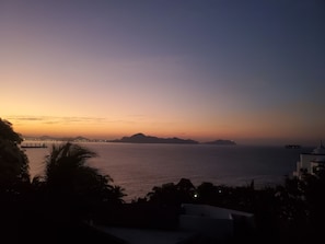 A coastal sunset view with distant landforms and a calm sea.