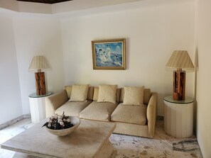A living room with a beige sofa, two side tables with lamps, a painting on the wall, and a bowl of flowers on a coffee table.