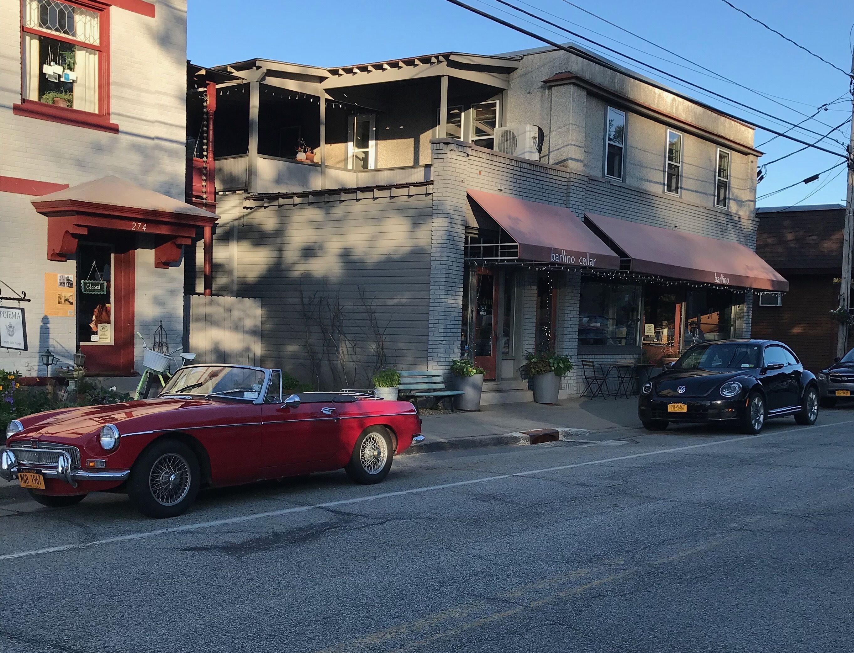 Ein rotes Cabriolet parkt auf einer Straße, davor ein schwarzes Auto und ein Gebäude mit der Aufschrift 'barvino Keller'.