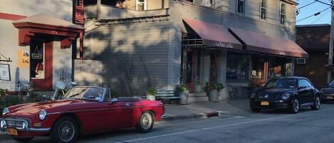 Un coche descapotable rojo estacionado en una calle, un coche negro adelante y un edificio con un letrero que dice 'barvino cellar'.