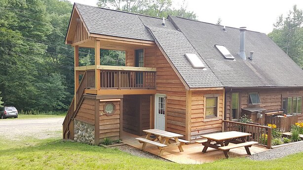 A two-story log cabin with a balcony, a patio with picnic tables, and a small outdoor kitchen. - Beautiful Rustic 4 bdr Chalet Made For Big Groups and Life Long Memories! (Great Valley)