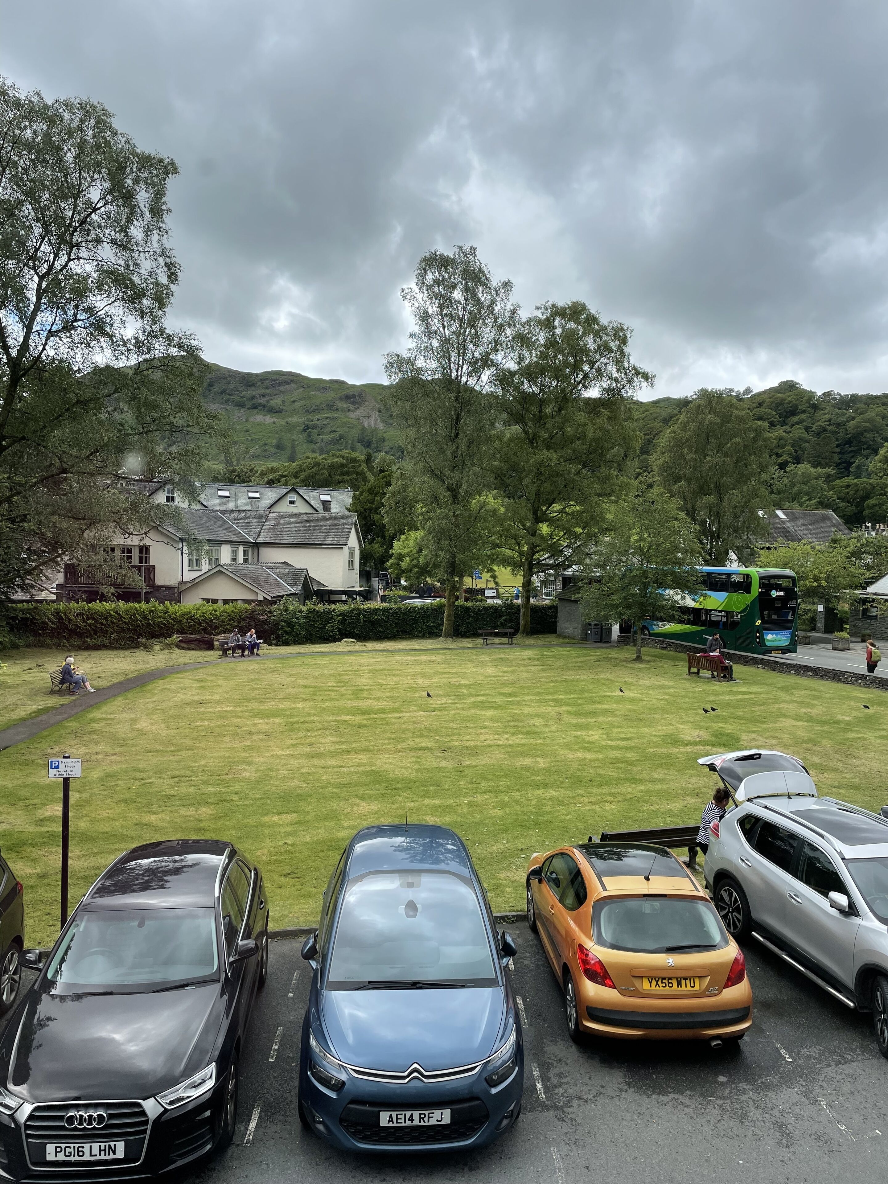 A parking area with several cars, a bus, and a grassy field with benches.