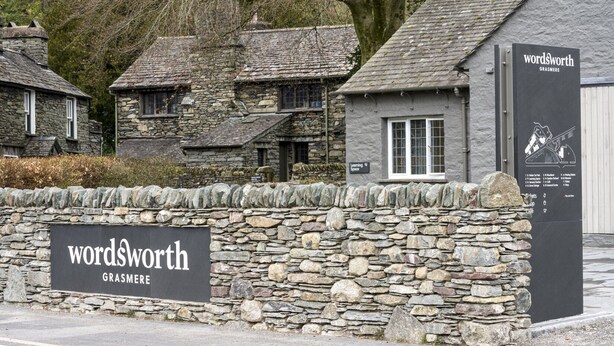 A stone wall with a sign for 'Wordsworth Grasmere' and a building with a slate roof. - Newly refurbished 2 bedroom, 2 bathroom apartment right in the heart of Grasmere (Grasmere)