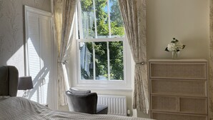 A bedroom with a large bed, a dresser, a chair, a window with curtains, and a chandelier. - Newly refurbished 2 bedroom, 2 bathroom apartment right in the heart of Grasmere (Grasmere)