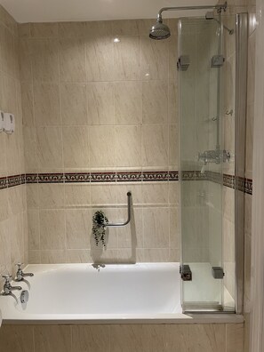 A bathroom with a glass-enclosed shower, a white bathtub with a handheld showerhead, and a decorative tile border.