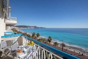 A balcony with a view of the beach and ocean, outdoor seating with striped chairs, and a table set for dining. - Horizon Blue Lux Apartment (Nice)